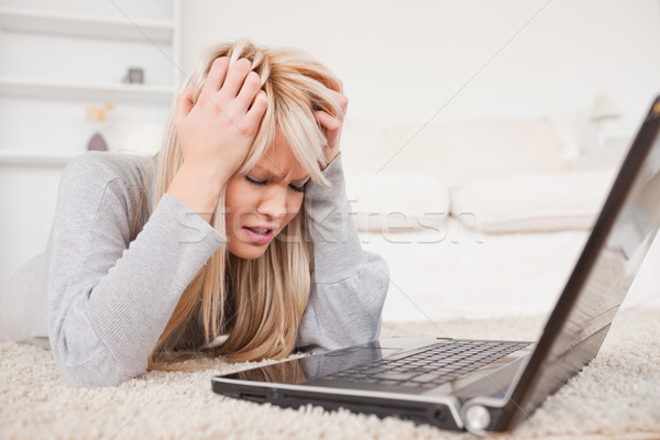 Attractive blond woman angry with her computer lying on a carpet in the living room Stock photo © wavebreak_media