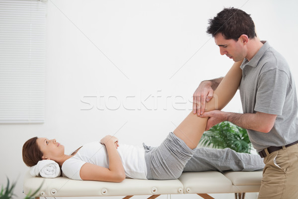 Stock photo: Physiotherapist massaging a leg while placing it on his shoulder in a room