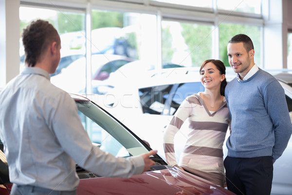 Stock photo: Smiling couple in a car shop with a car dealer
