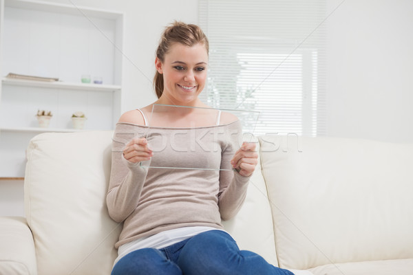 Woman holding a clear pane as a tablet pc while smiling and sitting on the sofa Stock photo © wavebreak_media