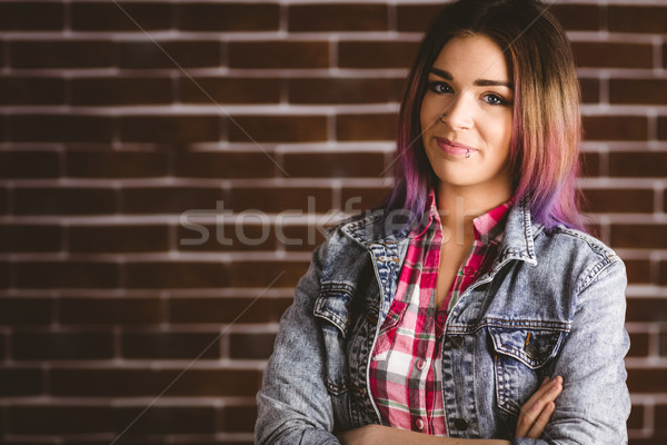 Stock photo: Smiling woman standing with arms crossed against brick wall