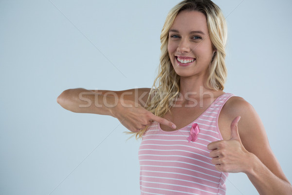 Stock photo: Portrait of smiling woman showing thumbs up while pointing on pink ribbon