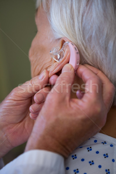 Stock photo: Doctor inserting hearing aid in senior patient ear