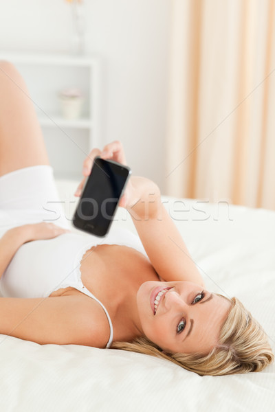 Portrait of a blonde woman showing her phone while lying on her bed Stock photo © wavebreak_media