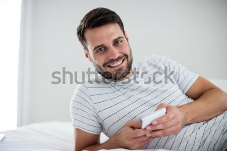 Stock photo: Portrait of a smiling man sitting on his bed while looking at the camera