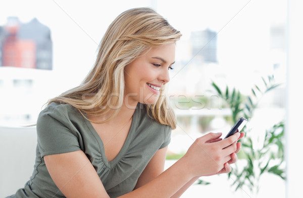 A woman turned to the side, smiles as she sits and uses her phone. Stock photo © wavebreak_media