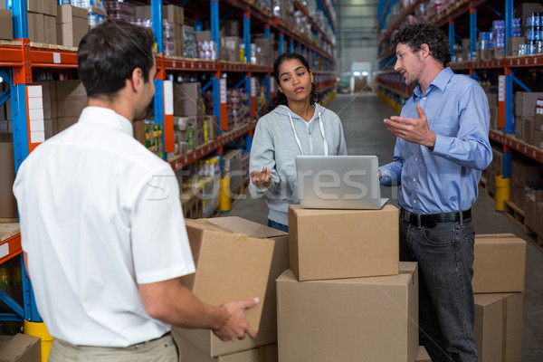 Stock photo: Warehouse manager carrying a box and his colleagues discussing
