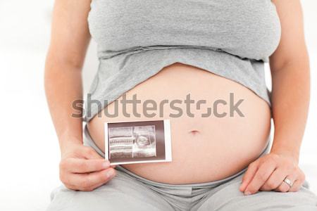 Stock photo: Pregnant woman showing an ultrasound scan while standing against a white background