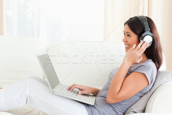 Stock photo: smiling woman sitting on sofa in livingroom wearing earphones 
