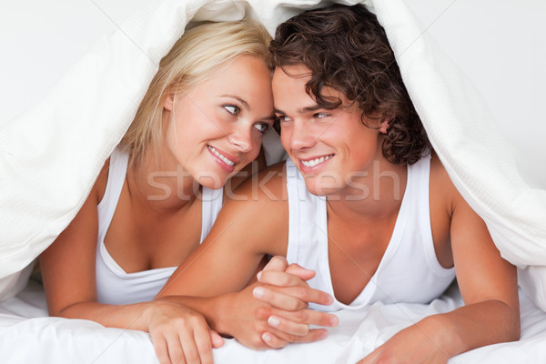 Stock photo: Portrait of an in love couple under a duvet in a bed