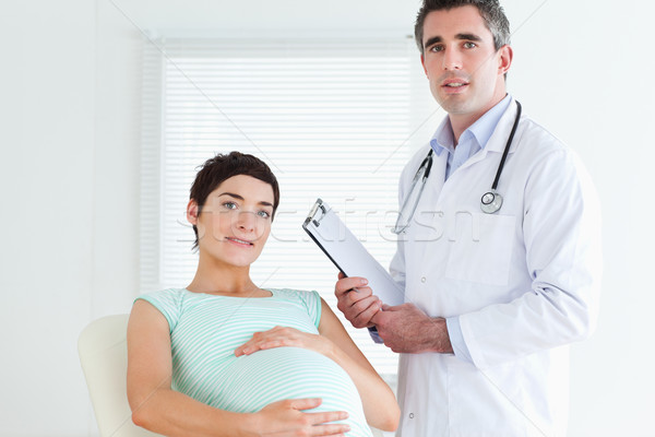 Stock photo: Male Doctor and pregnant patient looking at the camera in a room