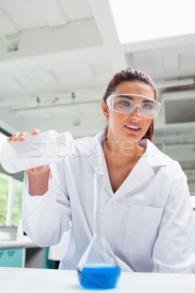 Portrait of a female science student pouring liquid with protective glasses while looking at the cam Stock photo © wavebreak_media