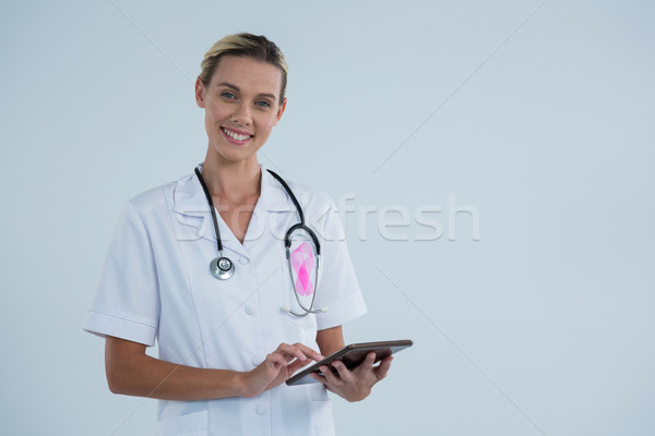 Stock photo: Portrait of female doctor with Breast Cancer Awareness ribbon using tablet computer