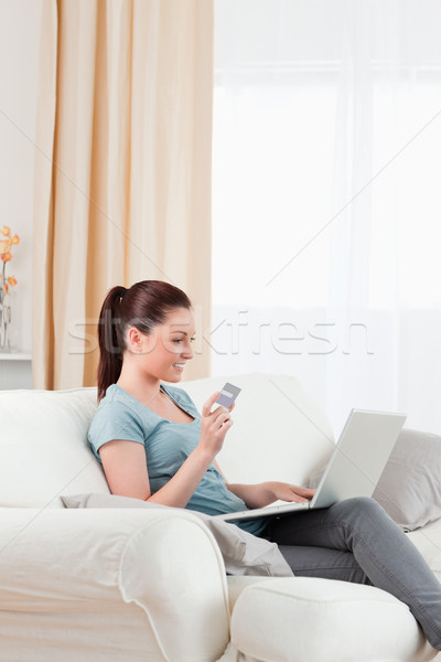 Stock photo: Cute woman making an online payment with her credit card while sitting on a sofa in the living room