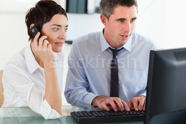 Stock photo: Businesswoman telephoning while her colleague is using a computer in an office