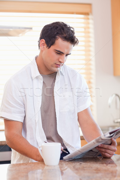 Stock photo: Young man doing crossword puzzle in the kitchen