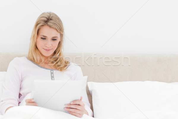 A woman sitting upright in bed with a tablet pc in front of her. Stock photo © wavebreak_media