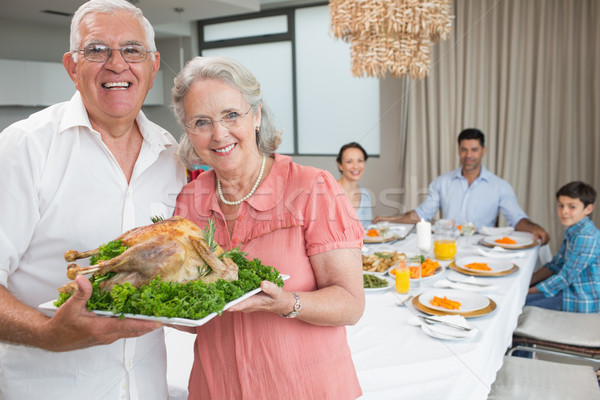 Grandparents holding chicken roast with family at dining table Stock photo © wavebreak_media