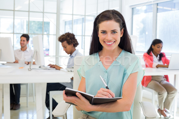 Attractive businesswomen writing in notebook with colleagues beh Stock photo © wavebreak_media