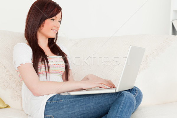 Stock photo: Beautiful red-haired woman relaxing with her laptop while sitting on a sofa in the living room