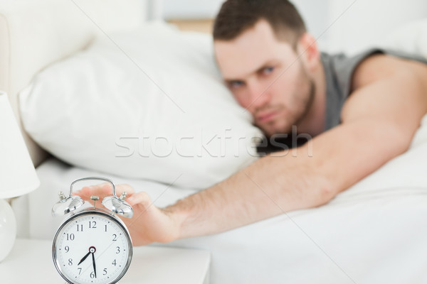 Unhappy man switching off his alarm clock in his bedroom Stock photo © wavebreak_media