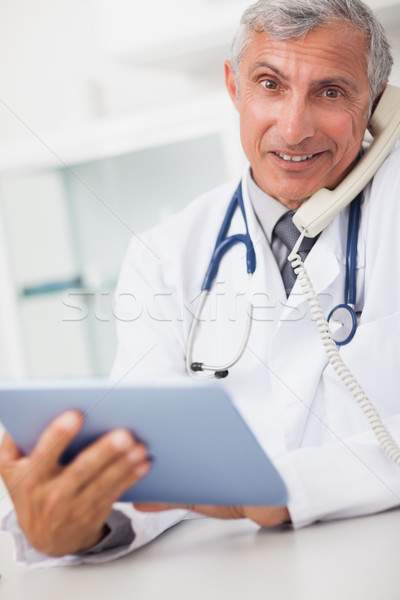 Smiling doctor holding a tablet computer and calling in medical office Stock photo © wavebreak_media