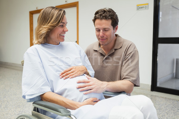 Pregnant woman and partner both touching her belly and smiling in hospital corridor Stock photo © wavebreak_media