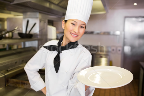 Stock photo: Smiling female cook holding empty plate in kitchen