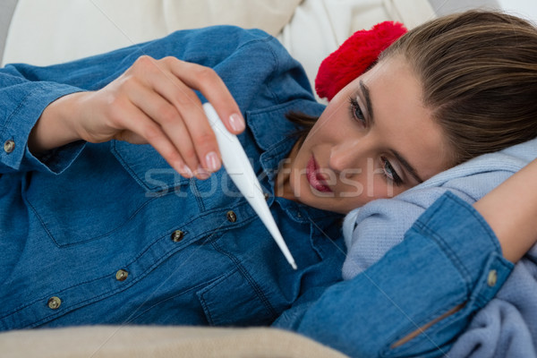 Stock photo: Woman checking thermometer while lying on sofa at home