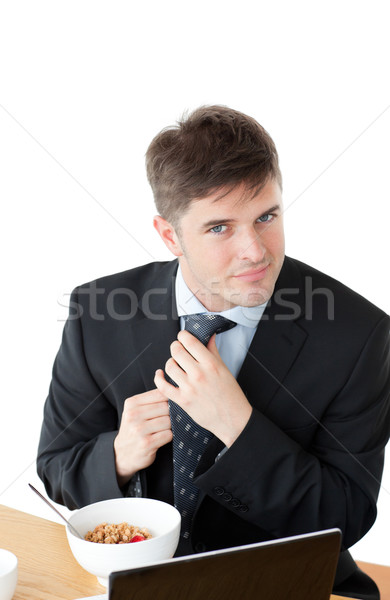 Elegant businessman having breakfast and touching his tie in front of his laptop against a white bac Stock photo © wavebreak_media