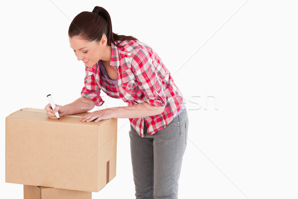 Stock photo: Attractive woman writing on cardboard boxes with a marker while standing against a white background