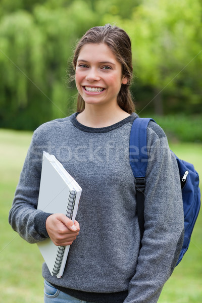 Teenager beaming while holding a notebook and standing upright in a park Stock photo © wavebreak_media