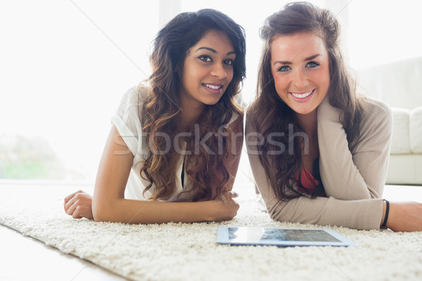 Stock photo: Two smiling friends looking at tablet computer while lying on the floor in a living room