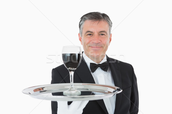 Smiling waiter holding a glass full of wine on a silver tray on white background Stock photo © wavebreak_media