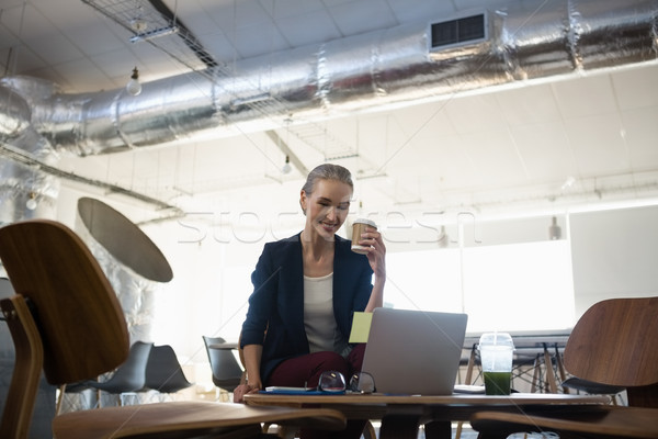 Businesswoman holding disposable cup while sitting at table in office Stock photo © wavebreak_media