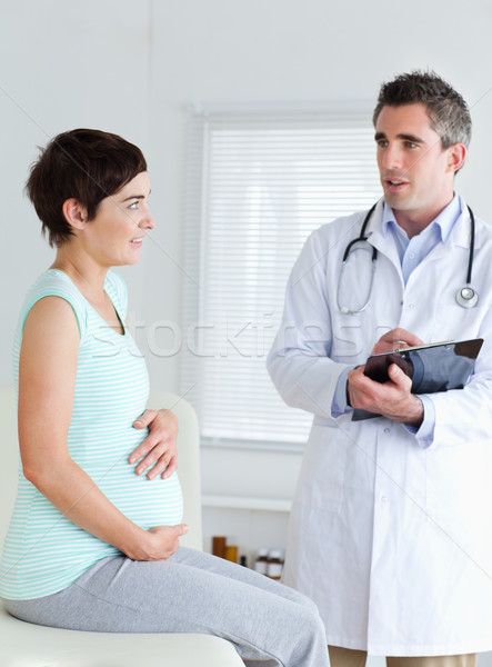 Sitting Pregnant woman touching her belly while talking to her doctor Stock photo © wavebreak_media