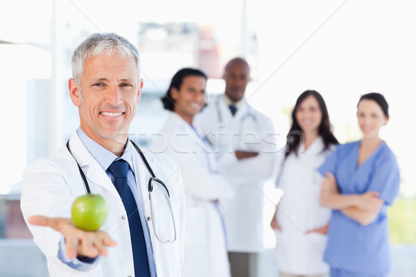 Stock photo: Smiling doctor holding an apple while his team is looking at him