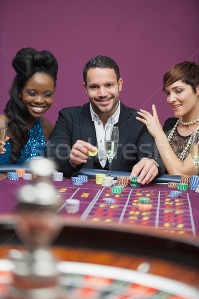 Stock photo: Man playing roulette with tow women either side in casino