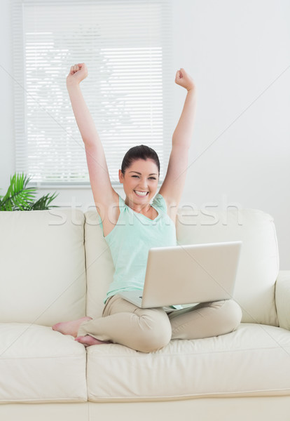 Woman sitting on the couch in a living room and being happy while raising her hands up with laptop Stock photo © wavebreak_media