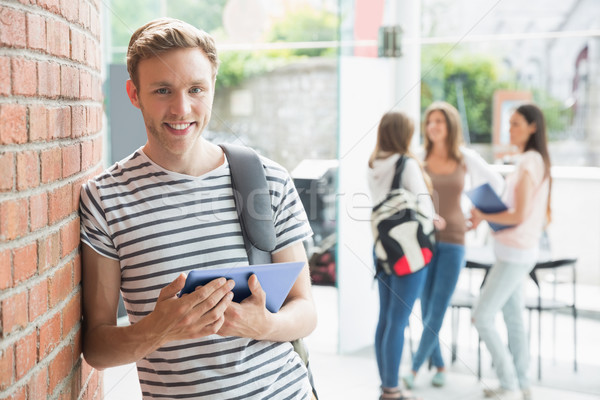 Handsome student smiling and holding tablet Stock photo © wavebreak_media
