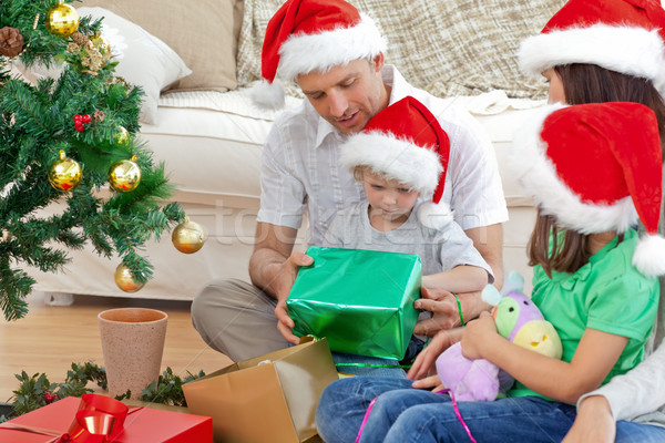Happy family looking at the little boy opening a christmas present in the living room Stock photo © wavebreak_media