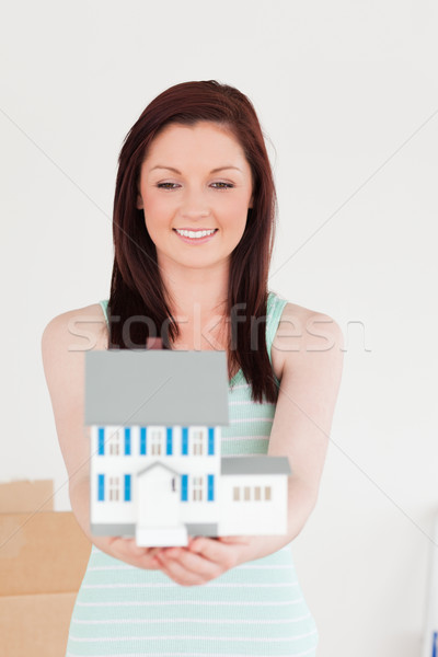 Stock photo: Good looking red-haired woman holding a miniature house while standing on the floor at home