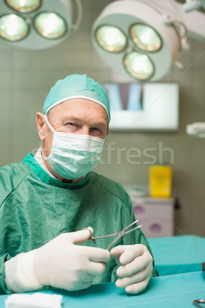 Stock photo: Smiling doctor holding scissors in a surgical room