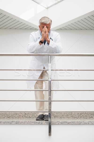 Worried doctor with face in hands leans against rail in hospital corridor Stock photo © wavebreak_media