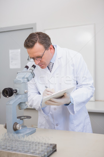Scientist analysing microscope writing on clipboard  Stock photo © wavebreak_media
