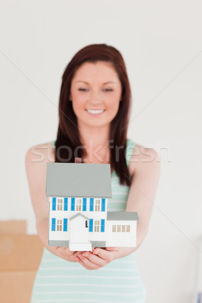 Stock photo: Pretty red-haired woman holding a miniature house while standing on the floor at home