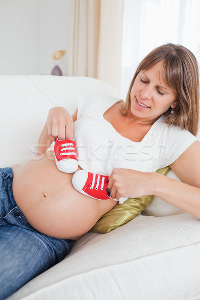 Charming pregnant woman playing with red baby shoes while lying on a sofa in her living room Stock photo © wavebreak_media