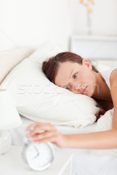 Sleepy red-haired woman lying in bed turning off alarm clock in her bedroom Stock photo © wavebreak_media