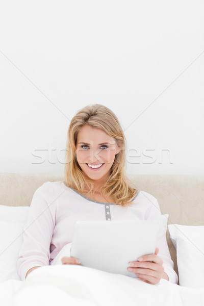 A centered shot of a woman with a tablet pc, looking forward and smiling while in bed. Stock photo © wavebreak_media