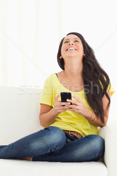 Happy Latino looking up while holding her smartphone being on a sofa Stock photo © wavebreak_media